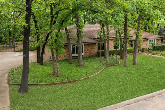 view of front of home featuring a tiled roof, driveway, a front yard, brick siding, and fence