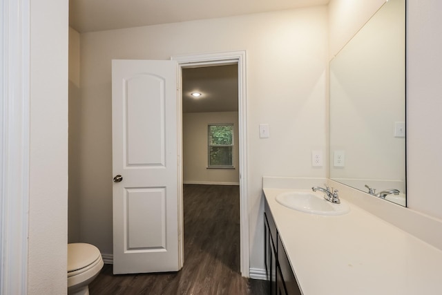 half bath featuring toilet, wood finished floors, vanity, and baseboards