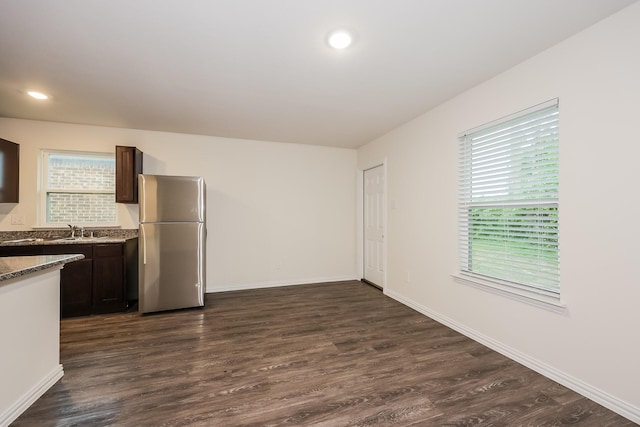 kitchen featuring dark wood finished floors, plenty of natural light, freestanding refrigerator, dark brown cabinets, and a sink