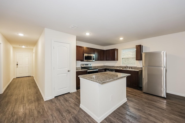 kitchen featuring a sink, appliances with stainless steel finishes, a kitchen island, dark brown cabinets, and dark wood finished floors