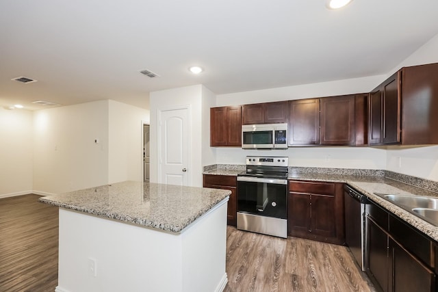 kitchen featuring light wood-style floors, appliances with stainless steel finishes, a kitchen island, a sink, and visible vents
