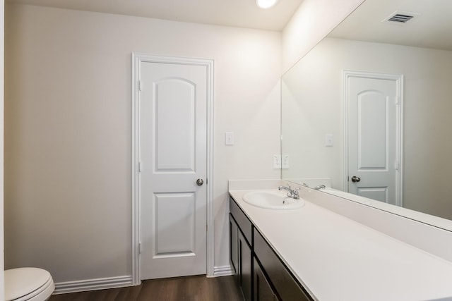 half bath with visible vents, baseboards, toilet, wood finished floors, and vanity