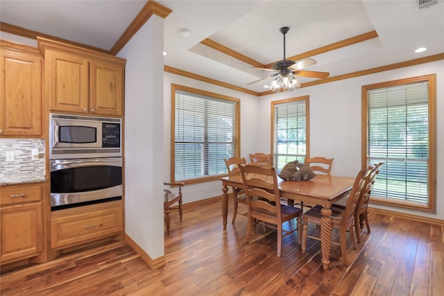 dining area with ornamental molding, a raised ceiling, a ceiling fan, and wood finished floors