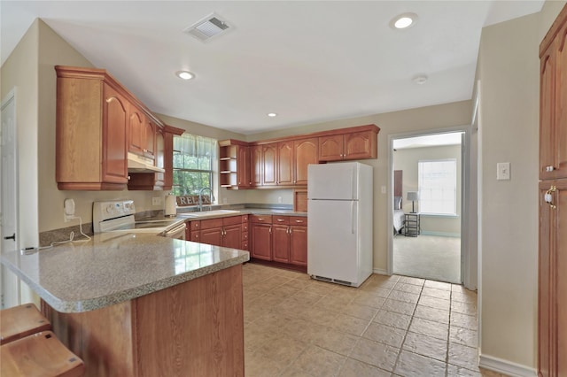 kitchen with visible vents, a sink, a peninsula, under cabinet range hood, and white appliances
