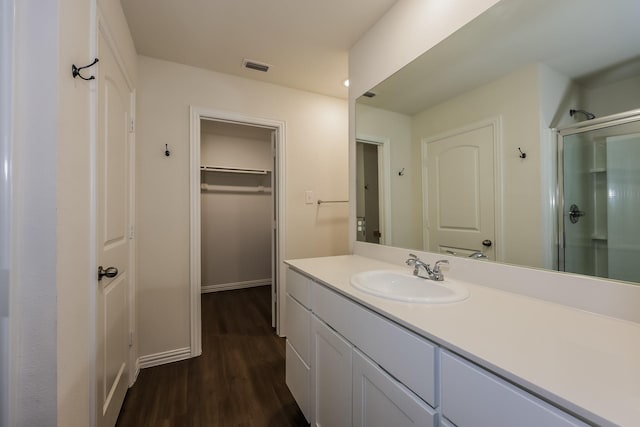 bathroom with vanity, wood finished floors, a spacious closet, visible vents, and a stall shower