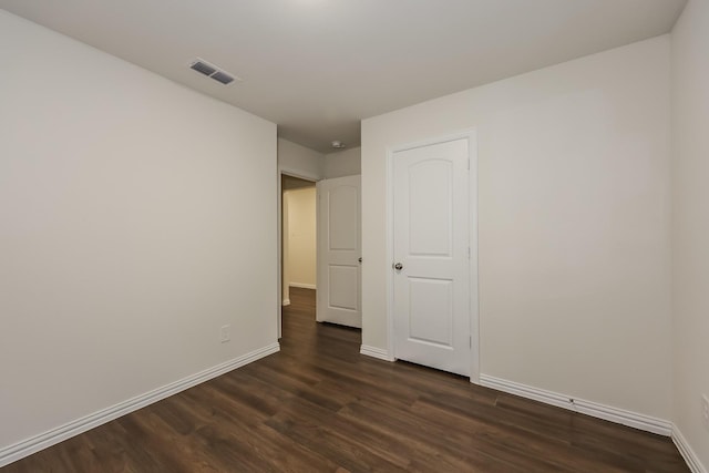 unfurnished room featuring baseboards, dark wood-type flooring, and visible vents
