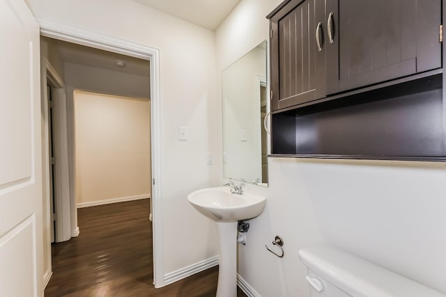 half bath with baseboards, toilet, and wood finished floors