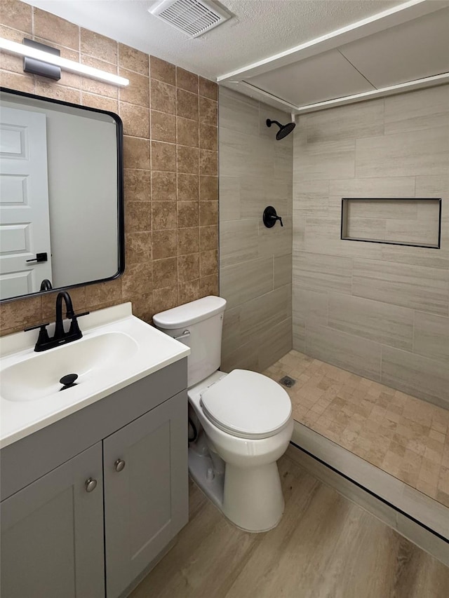 1830 Bosque Dr, Garland, TX 75040 - full bathroom featuring tiled shower, vanity, wood finished floors, a textured ceiling, and tile walls