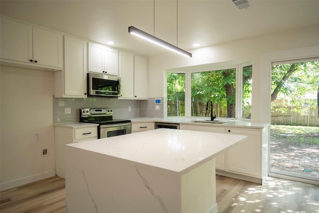 1830 Bosque Dr, Garland, TX 75040 - kitchen featuring appliances with stainless steel finishes, light wood-style flooring, tasteful backsplash, a kitchen island, and white cabinets