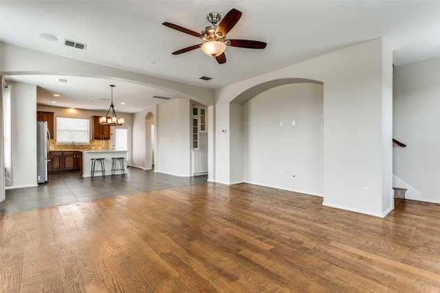 unfurnished living room featuring dark wood finished floors, visible vents, and ceiling fan with notable chandelier