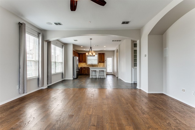 unfurnished living room featuring visible vents, ceiling fan with notable chandelier, and dark wood-style flooring