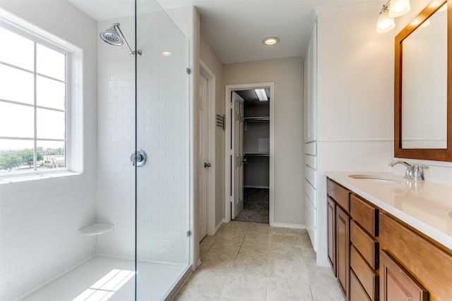bathroom with a spacious closet, a tile shower, tile patterned flooring, and vanity