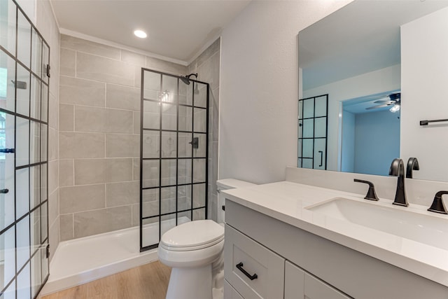 full bath featuring a tile shower, toilet, wood finished floors, vanity, and a ceiling fan