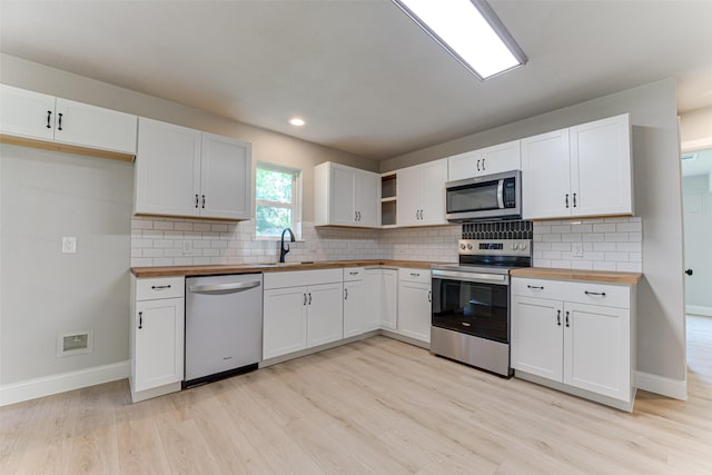 kitchen featuring a sink, stainless steel appliances, light wood-style flooring, baseboards, and butcher block counters