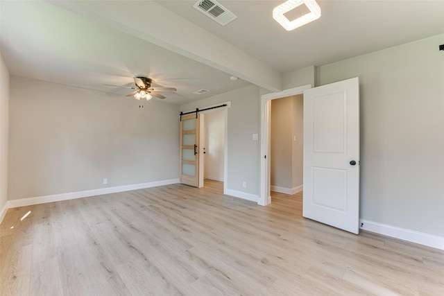 unfurnished bedroom with a barn door, a ceiling fan, visible vents, light wood-style flooring, and baseboards