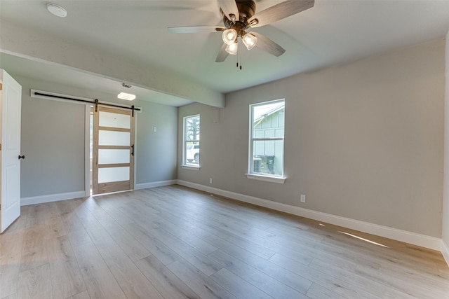empty room featuring a barn door, ceiling fan, light wood-style flooring, and baseboards