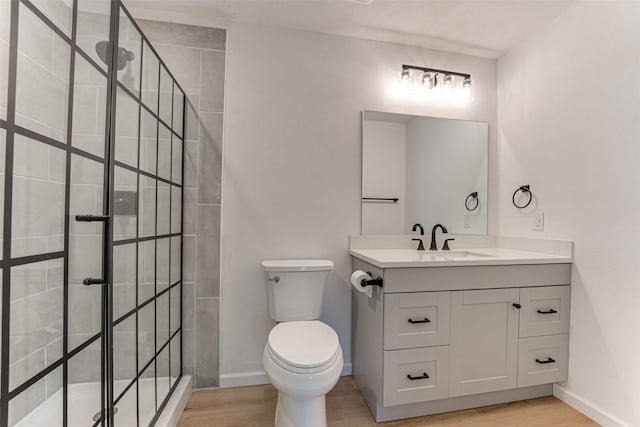 bathroom with a tile shower, baseboards, toilet, wood finished floors, and vanity