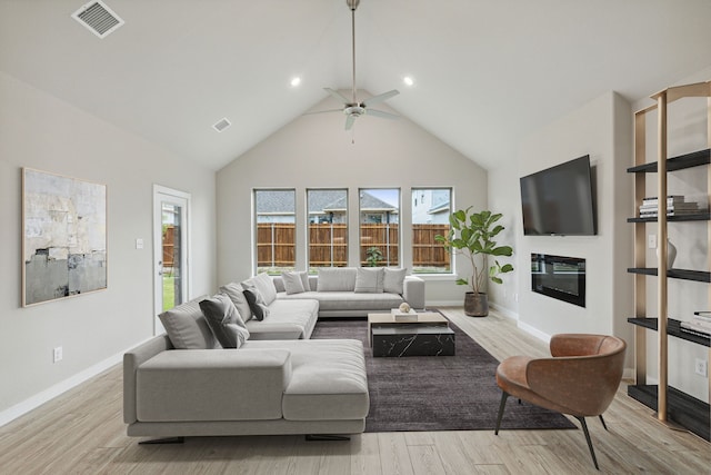 living area featuring visible vents, ceiling fan, a glass covered fireplace, wood finished floors, and high vaulted ceiling