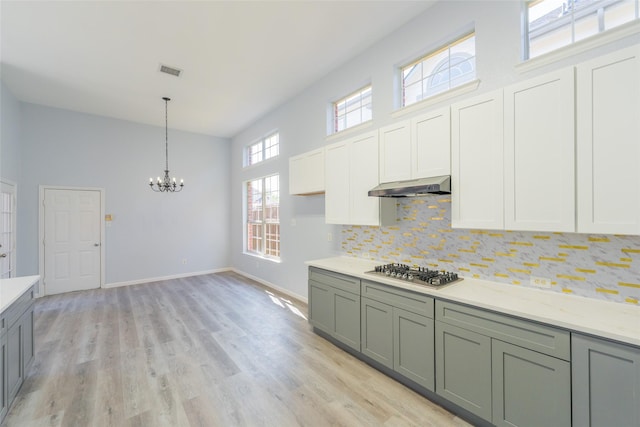 7404 Maybrook Ct, Plano, TX 75024 - kitchen featuring stainless steel gas cooktop, a chandelier, under cabinet range hood, backsplash, and hanging light fixtures