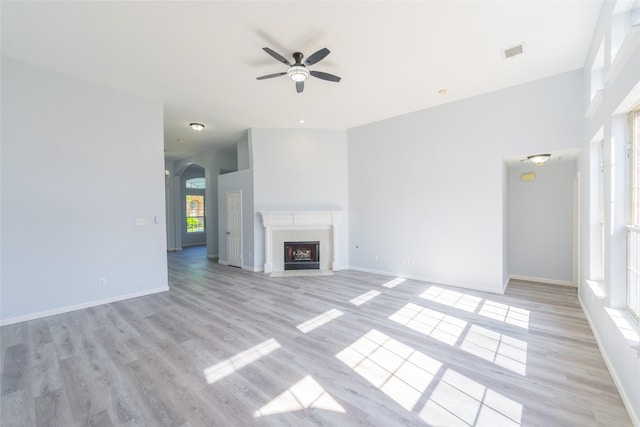 7404 Maybrook Ct, Plano, TX 75024 - unfurnished living room featuring ceiling fan, light wood-style flooring, baseboards, a fireplace with flush hearth, and arched walkways