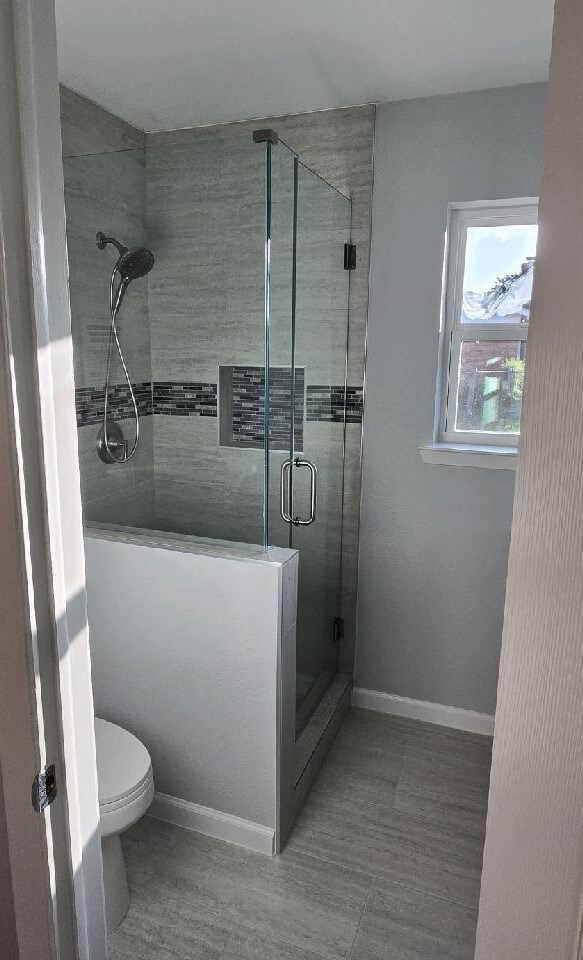 bathroom with toilet, a shower stall, and baseboards