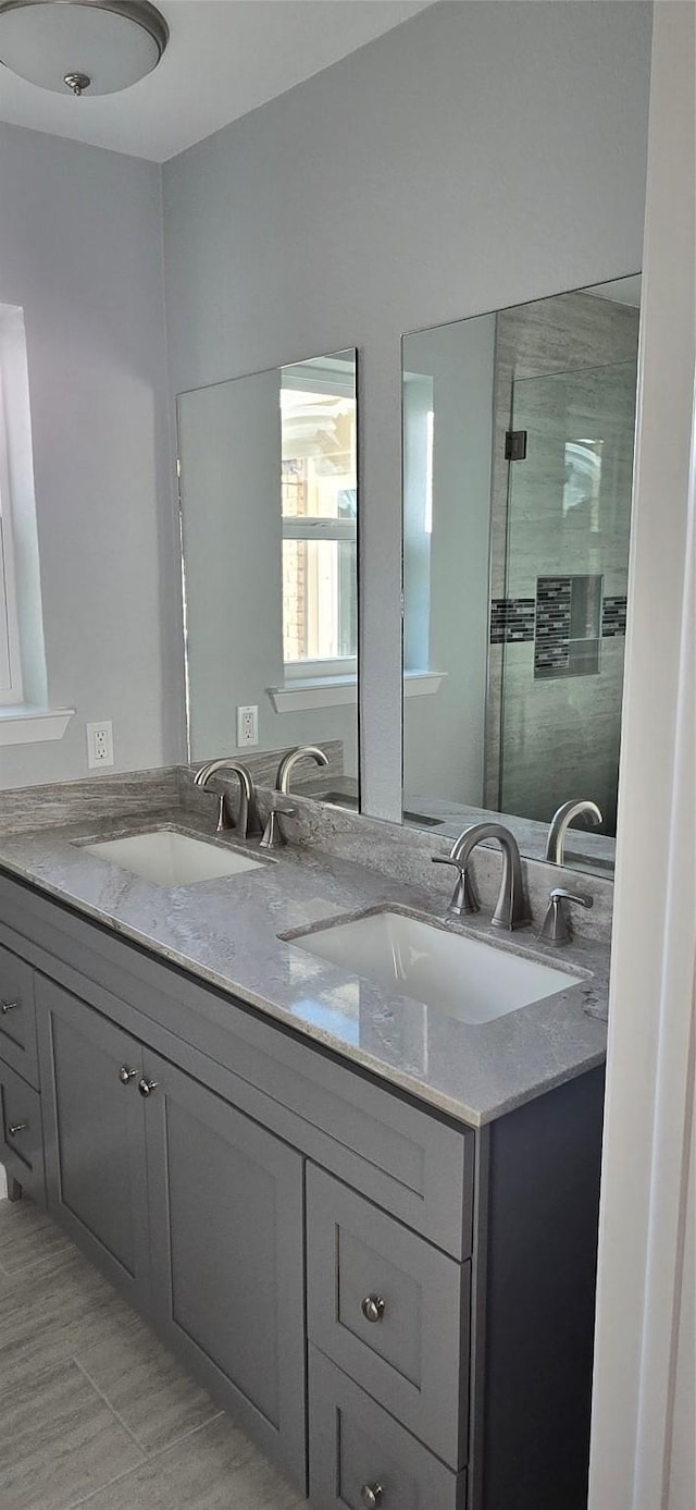full bathroom featuring tiled shower, double vanity, and a sink