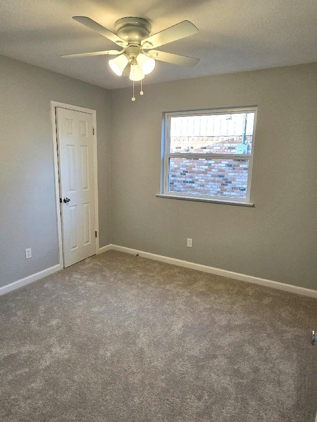 carpeted empty room featuring a ceiling fan and baseboards