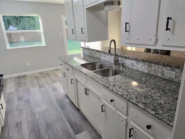 kitchen featuring white cabinetry, light stone counters, a sink, baseboards, and light wood-type flooring