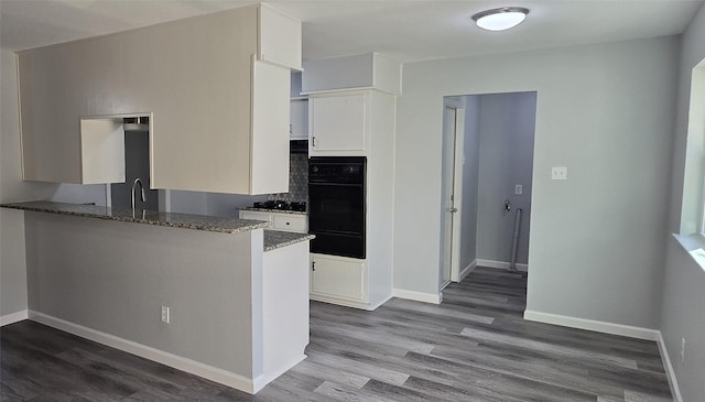 kitchen featuring dark stone counters, baseboards, black oven, white cabinets, and wood finished floors