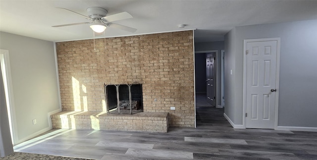 unfurnished living room with wood finished floors, a ceiling fan, baseboards, and a brick fireplace