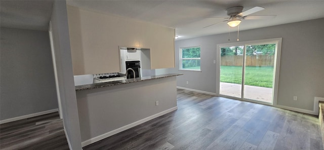 kitchen with black oven, stone counters, ceiling fan, baseboards, and dark wood-type flooring