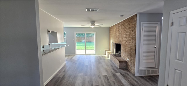 unfurnished living room with visible vents, ceiling fan, baseboards, a brick fireplace, and wood finished floors