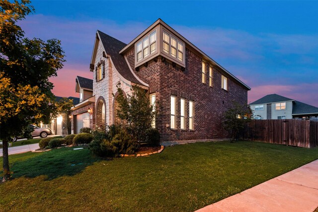 view of side of home featuring fence, a yard, brick siding, and a garage