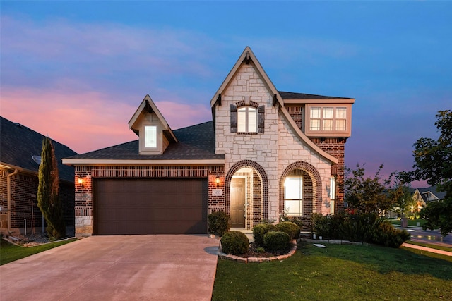 french country home featuring concrete driveway, an attached garage, a front lawn, and stone siding