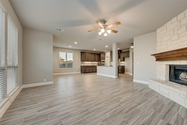 unfurnished living room featuring a stone fireplace, light wood finished floors, baseboards, visible vents, and a ceiling fan