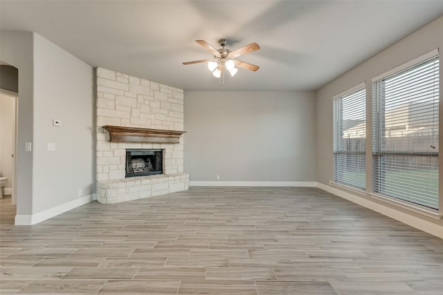 unfurnished living room with a ceiling fan, light wood finished floors, a stone fireplace, and baseboards