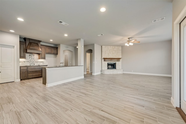 kitchen featuring arched walkways, custom exhaust hood, decorative backsplash, a ceiling fan, and open floor plan