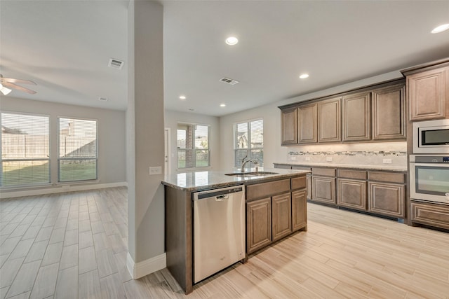 kitchen with a sink, stainless steel appliances, visible vents, light wood-style flooring, and light stone counters