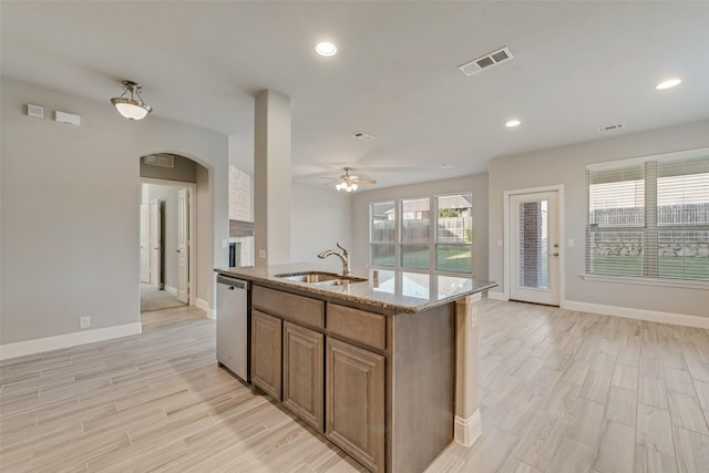 kitchen featuring stainless steel dishwasher, a sink, ceiling fan, arched walkways, and light wood finished floors