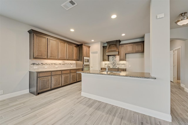 kitchen with custom exhaust hood, appliances with stainless steel finishes, decorative backsplash, and light wood-style floors
