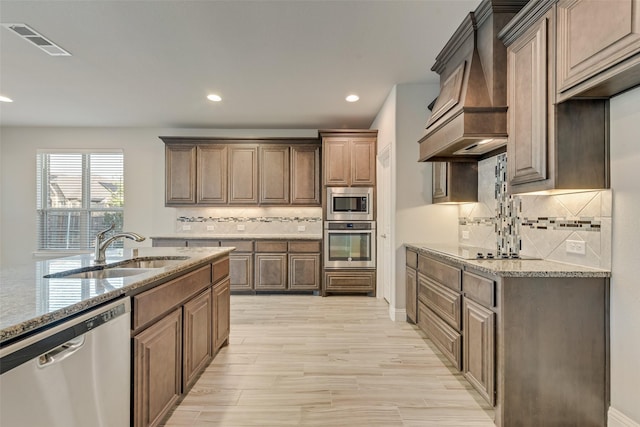 kitchen with custom exhaust hood, light stone counters, stainless steel appliances, a sink, and visible vents