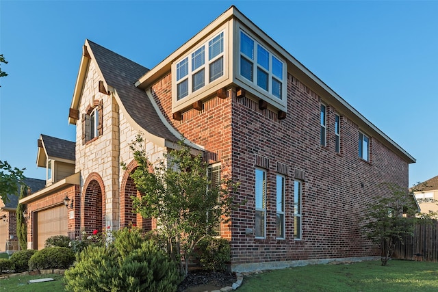 view of side of home with brick siding, roof with shingles, fence, and an attached garage