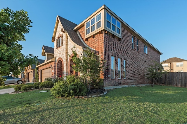 view of side of property featuring fence, a yard, an attached garage, and brick siding