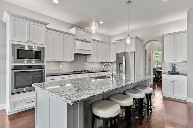 kitchen featuring dark wood-style floors, recessed lighting, a sink, arched walkways, and appliances with stainless steel finishes