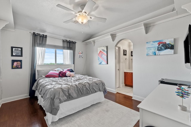 bedroom featuring connected bathroom, a ceiling fan, baseboards, arched walkways, and wood finished floors