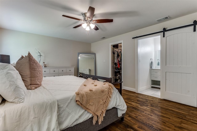 bedroom with a barn door, visible vents, a spacious closet, wood finished floors, and ensuite bathroom