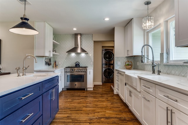 kitchen featuring wall chimney range hood, stacked washer and dryer, high end stainless steel range oven, a sink, and blue cabinetry