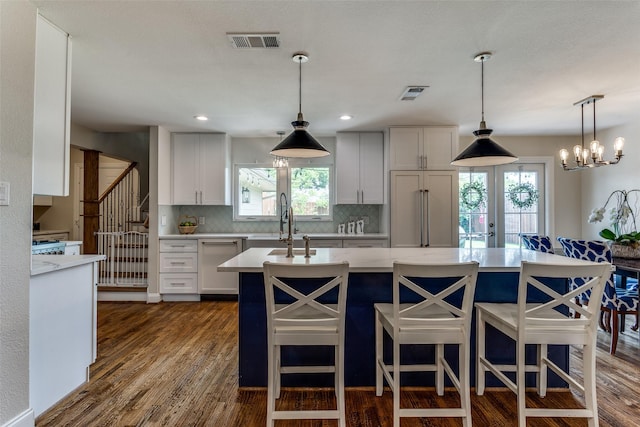 kitchen featuring visible vents, an island with sink, backsplash, and dishwasher
