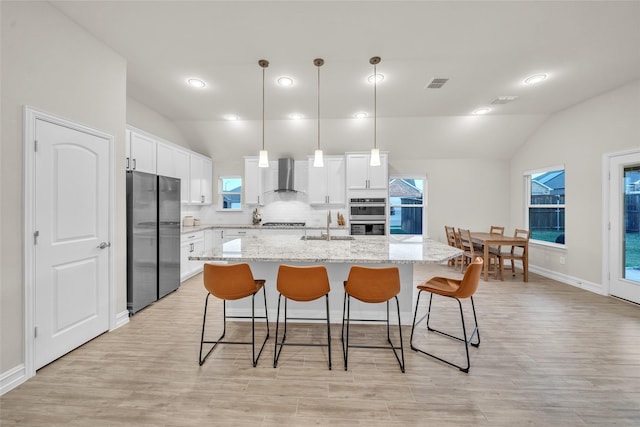 kitchen with tasteful backsplash, stainless steel appliances, a sink, wall chimney exhaust hood, and lofted ceiling