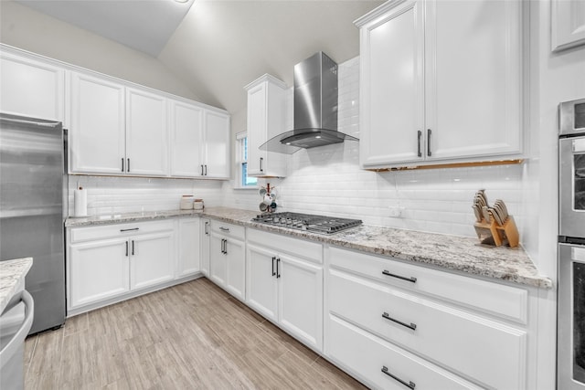 kitchen featuring stainless steel appliances, backsplash, vaulted ceiling, and wall chimney exhaust hood